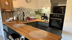 A modern kitchen with a wooden countertop, two chairs, a sink, a microwave, and an oven. - Air-conditioned apartment, terrace - 4 guests (Port Camargue)
