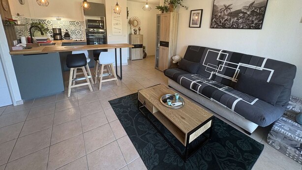 A modern living room with a sofa, a coffee table, and a kitchen area with bar stools. - Air-conditioned apartment, terrace - 4 guests (Port Camargue)