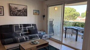 A living room with a sofa, a coffee table, and a sliding glass door leading to an outdoor dining area. - Air-conditioned apartment, terrace - 4 guests (Port Camargue)