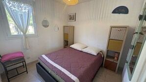 A bedroom with a bed, a bedside table, a chair, a wardrobe, and a window with curtains. - Air-conditioned apartment, terrace - 4 guests (Port Camargue)