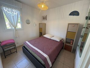 Een slaapkamer met een bed, nachtkastje, stoel, kledingkast en raam met gordijnen.