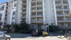A multi-story residential building with balconies, a parking area, and a small entrance with a door. - Air-conditioned apartment, terrace - 4 guests (Port Camargue)