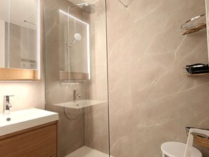 Ein modernes Badezimmer mit einer gläsernen Duschkabine, einem Waschtisch mit Spiegel und einer Toilette.