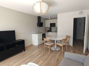 Ein modernes Wohnzimmer mit Flachbildfernseher, einer Couch und einem Essbereich mit rundem Tisch und Stühlen.