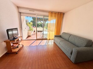 Ein Wohnzimmer mit einer Couch, einem Fernseher auf einem Holzschrank und einer Glastür, die zu einem Außenbereich führt.
