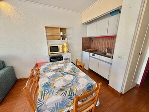 Ein kleines Zimmer mit einem Bett, einer Kochnische, einer Mikrowelle, einer Kaffeemaschine und einem Sessel.