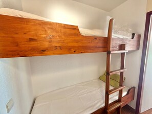 Ein Etagenbett mit Holzrahmen und einer Leiter, eine weiße Matratze und eine Plastiktüte im oberen Bett.