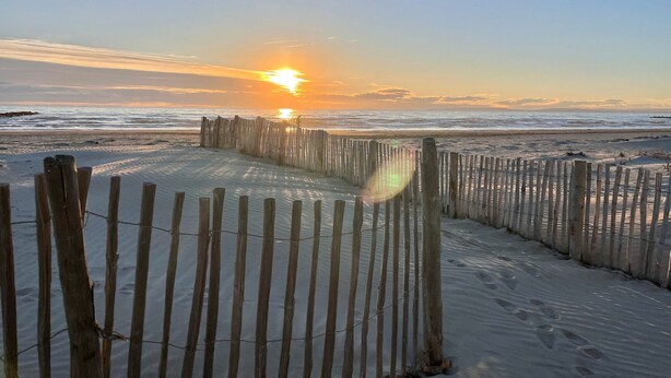 Ein Holzzaun am Strand, im Hintergrund ein Sonnenuntergang.