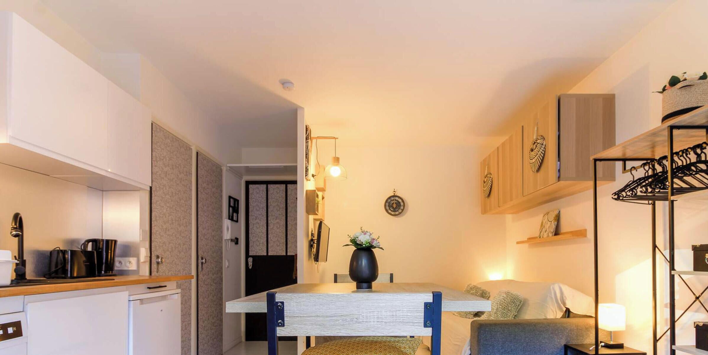 A compact living space with a kitchenette, a dining area, and a seating area with a sofa and a lamp.