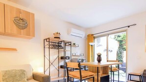 Un espace de vie compact comprenant une table à manger, des chaises, un canapé, une armoire intégrée, une étagère et une fenêtre donnant sur un paysage verdoyant.