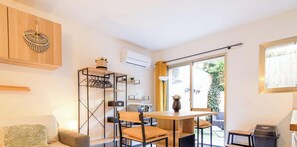 Ein kompakter Wohnraum mit Esstisch, Stühlen, einer Couch, einem Einbauschrank, einem Regal und einem Fenster mit Blick auf Grünflächen.