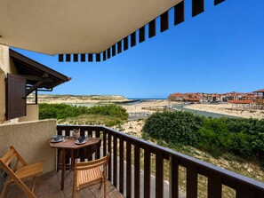 Ein Balkon mit Tisch und Stühlen, der Blick auf einen Strand und Gebäude bietet.