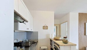 Eine kompakte Küche mit weißen Schränken, einer Edelstahl-Spüle und einer kleinen Arbeitsplatte mit Krug und Korb.