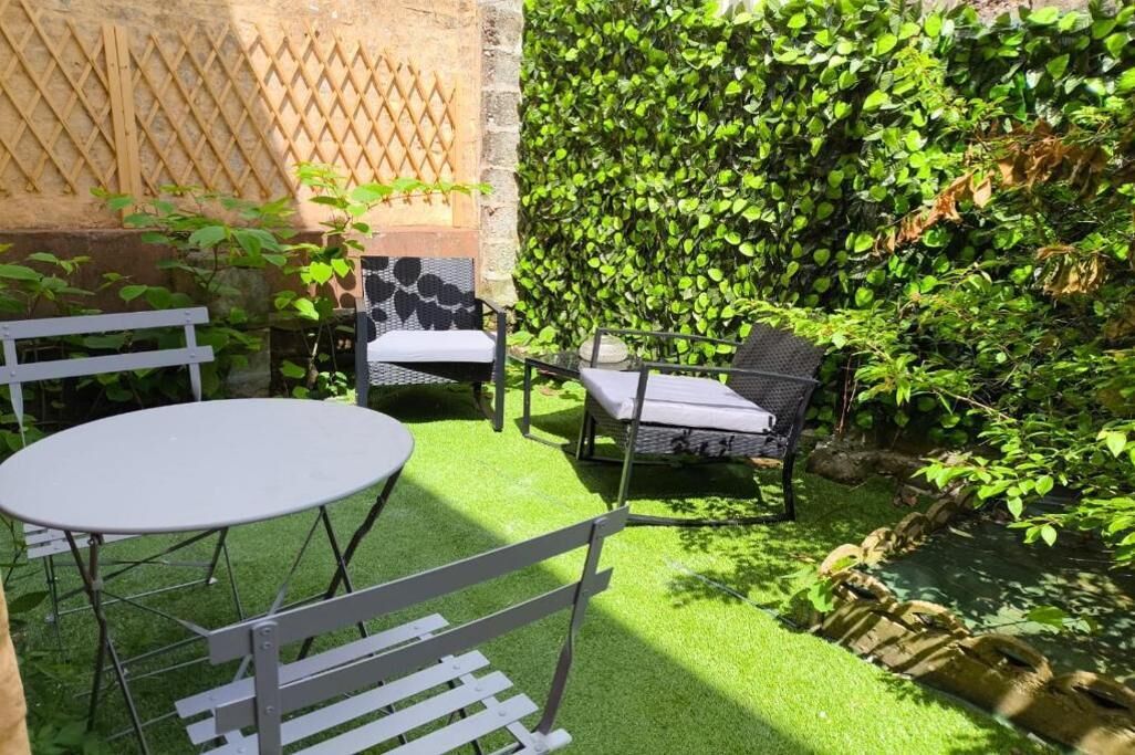 Une terrasse avec une table ronde et deux chaises, entourée d’un luxuriant feuillage verdoyant et d’un mur de pierre.