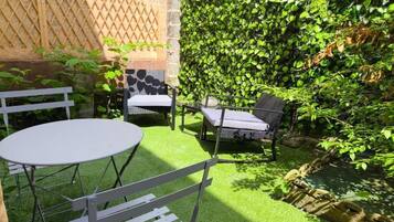 Une terrasse avec une table ronde et deux chaises, entourée d’un luxuriant feuillage verdoyant et d’un mur de pierre.