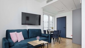 Un salon moderne avec un canapé bleu, une petite table en bois et un téléviseur à écran plat fixé au mur.