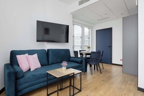 Ein modernes Wohnzimmer mit einem blauen Sofa, einem kleinen Holztisch und einem flachbildfernseher an der Wand.