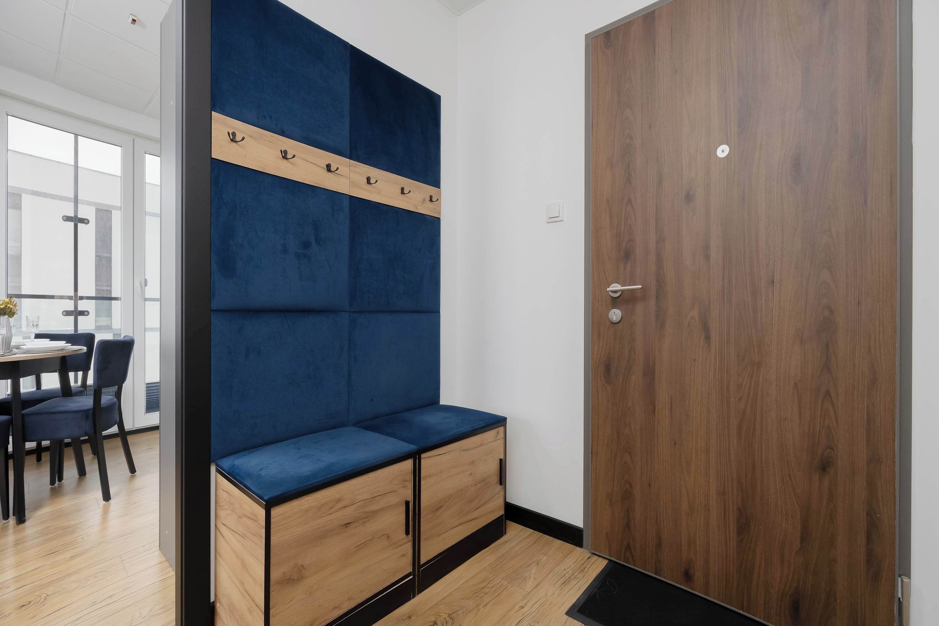 Een moderne kamer met een blauwe gestoffeerde bank, houten kasten, een houten deur en een eethoek met stoelen en een tafel.
