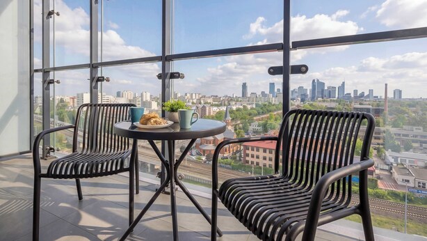 Un balcon avec deux chaises, une petite table sur laquelle se trouvent une tasse et une plante, et une vue sur la ville.