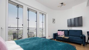 Une chambre moderne avec un grand lit, un canapé, une télévision et un balcon offrant une vue sur la ville.