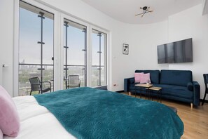 Ein modernes Schlafzimmer mit einem großen Bett, einer Couch, einem Fernseher und einem Balkon mit Blick auf die Stadt.