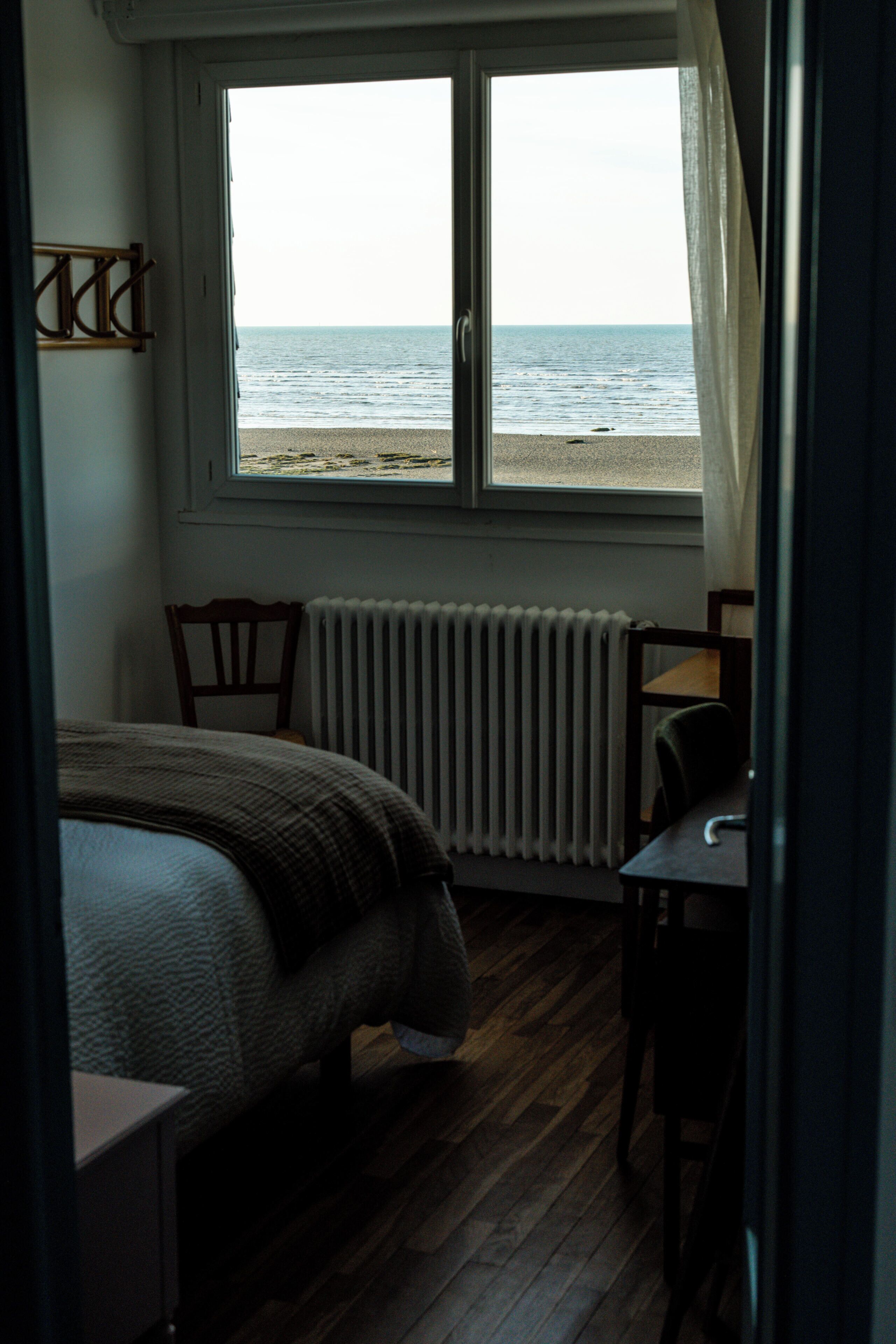 Une chambre à coucher comprenant un lit, une chaise, une table, une fenêtre donnant sur la plage et un radiateur.