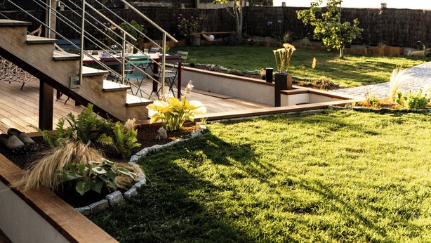 Une maison moderne dotée d’une terrasse en bois, d’un espace salon extérieur et d’une pelouse bien entretenue.