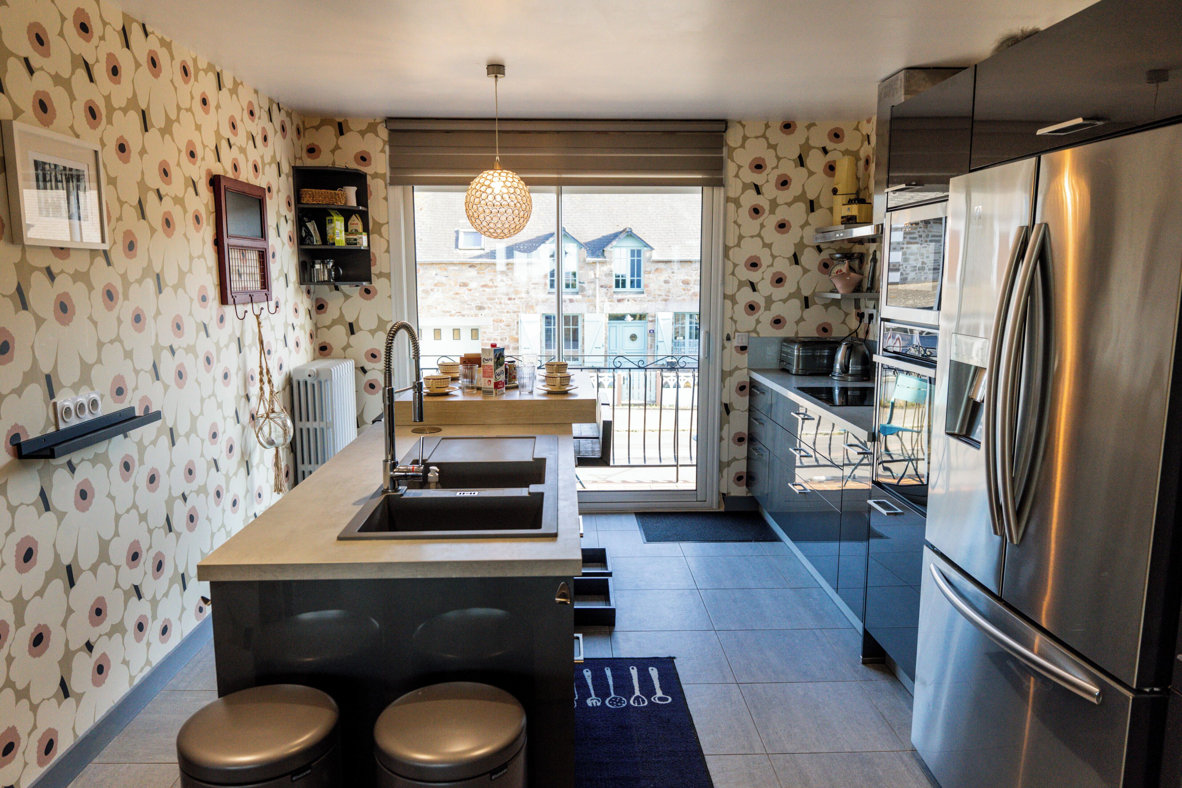 A modern kitchen with a stainless steel refrigerator, a built-in oven, and a large window overlooking a balcony.
