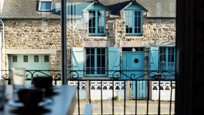 Une vue à travers la fenêtre d’un bâtiment en pierre, doté de nombreuses fenêtres et d’un balcon.