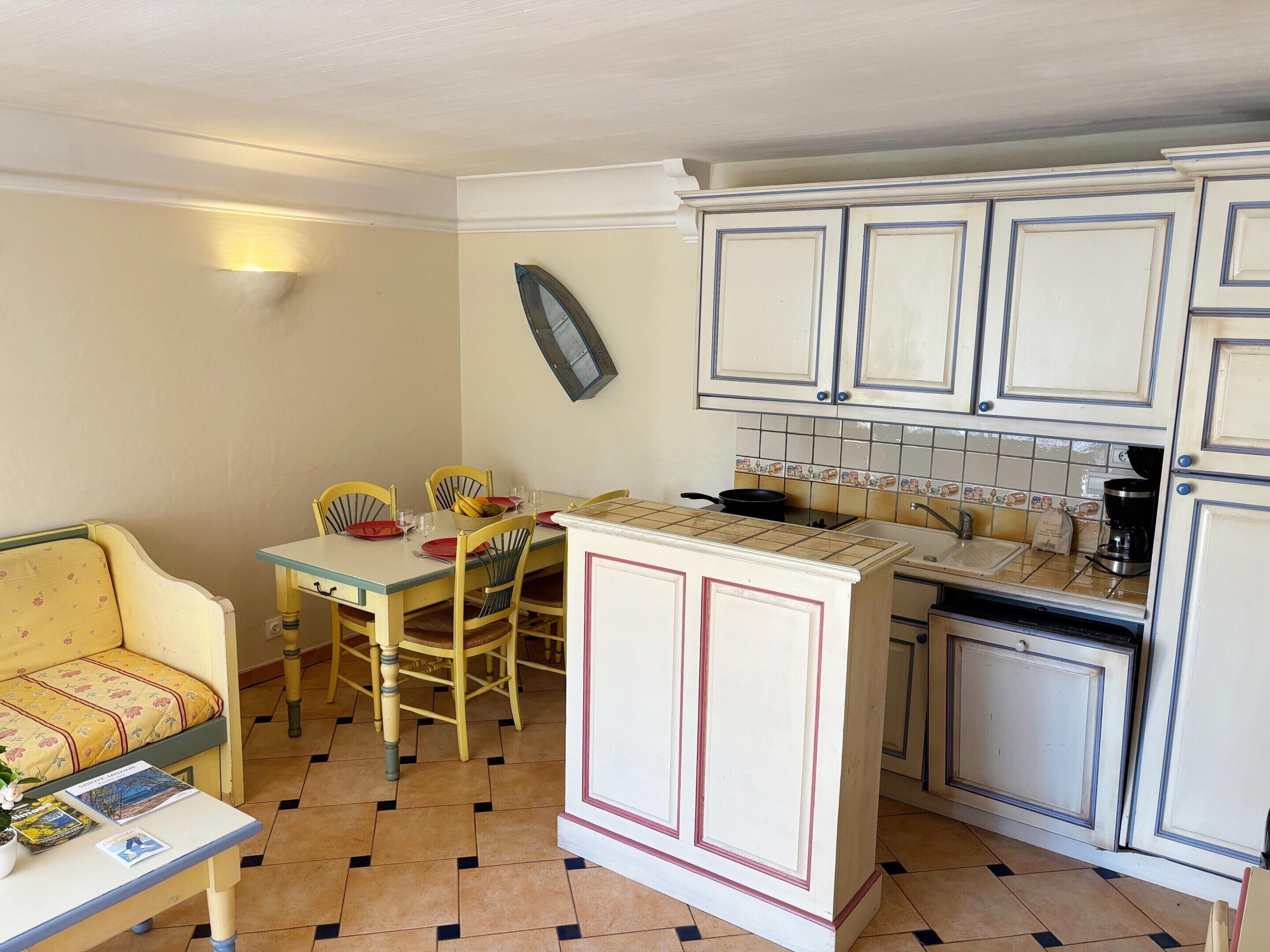 A compact kitchen with a dining area, featuring a tiled backsplash, a coffee maker, and a small refrigerator.