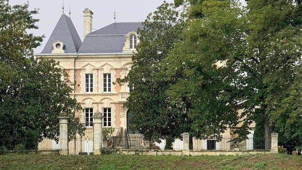 Un grande edificio storico con una torre imponente, circondato da vegetazione rigogliosa e una superficie d'acqua.