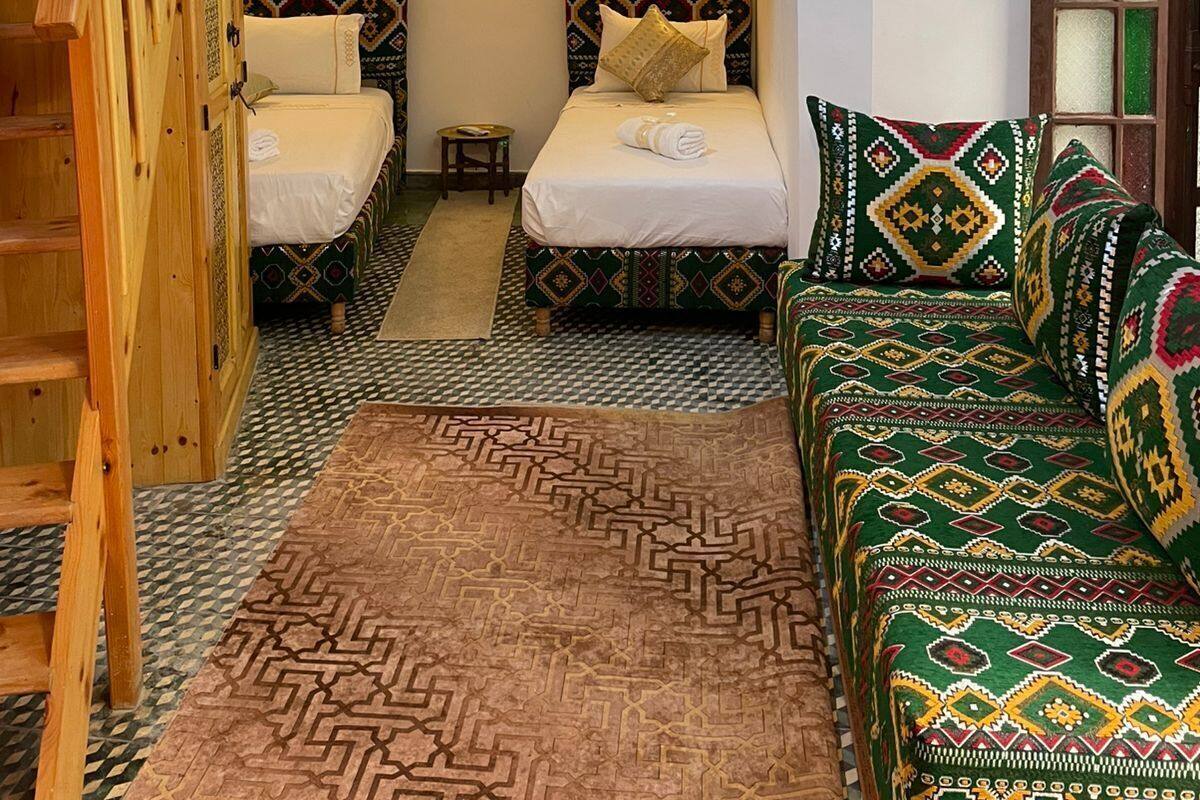 A room with a bunk bed, two single beds, a sofa, a patterned rug, and a wooden staircase.