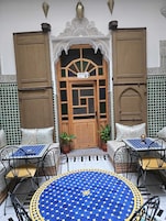 Um interior tradicional marroquino com uma porta de madeira, azulejos estampados e uma mesa azul com cadeiras.