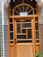 Uma porta de madeira com uma placa indicando 'TAFILAT N°231' e intrincados padrões geométricos nas paredes ao redor.