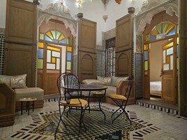 Um quarto com portas de madeira ornamentadas, chão quadriculado e uma mesa redonda com cadeiras.