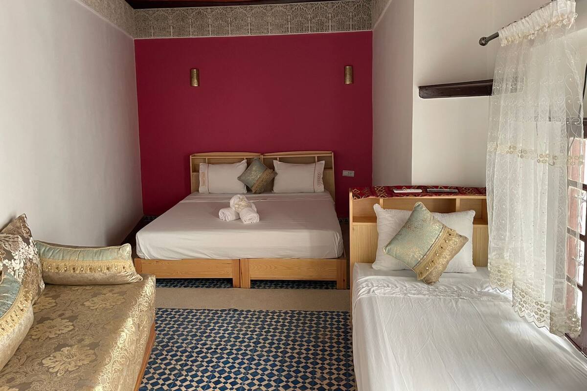 A room with a bed, two bedside tables, a wooden headboard, a patterned floor, and a red accent wall.
