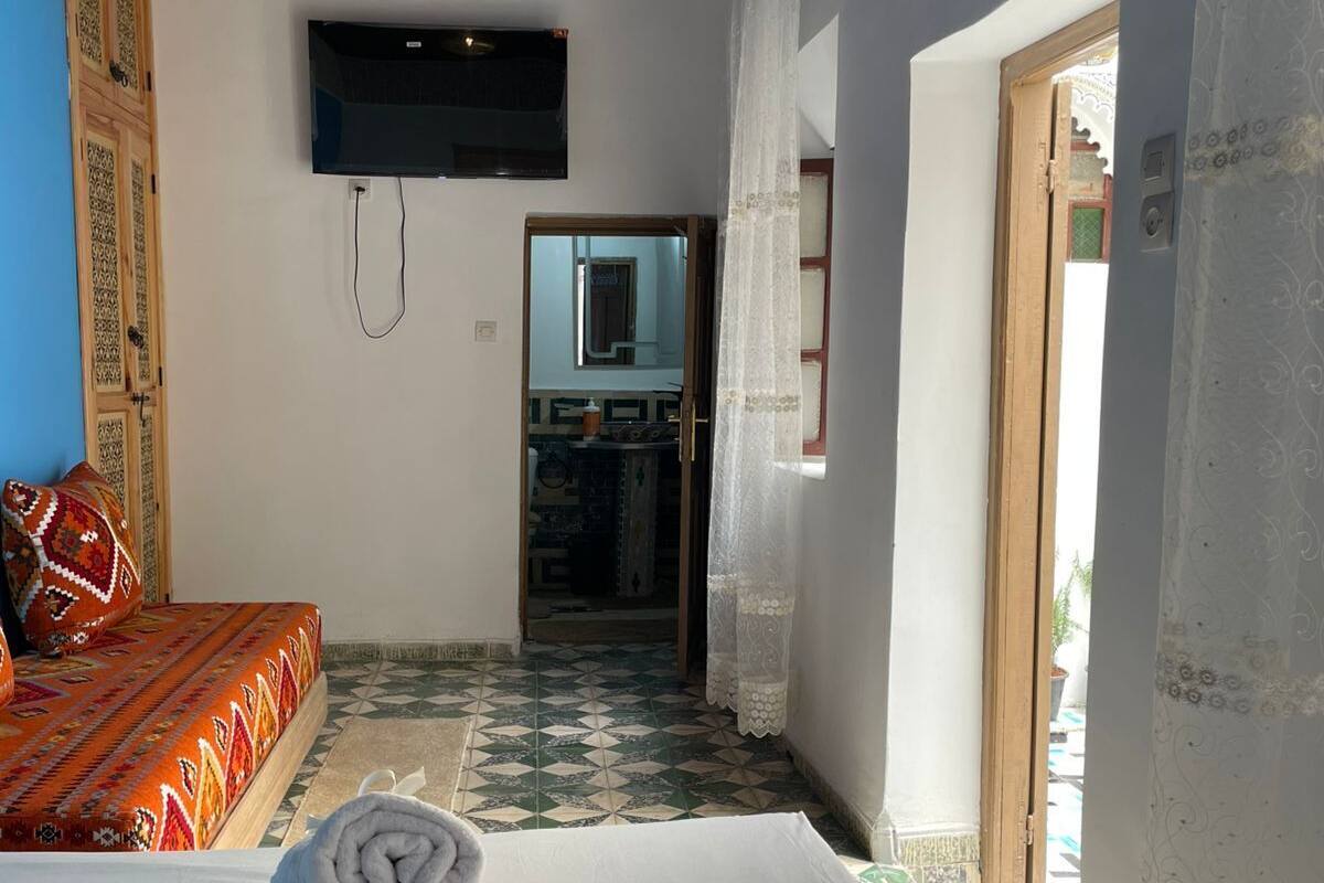 A bedroom with a bed, a TV, and a view of the outside.
