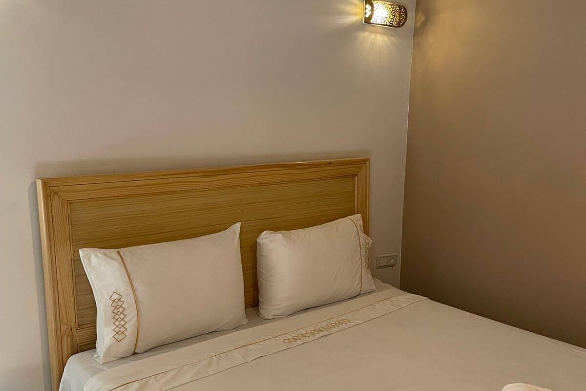 A neatly made bed with a wooden headboard, a bedside table with a lamp, and a wall-mounted light fixture.