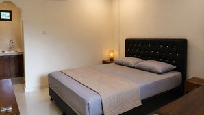 A bedroom with a bed, bedside table, nightstand, and a small window. - Puri Kawan Guesthouse (Denpasar)