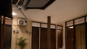 A hallway with a potted plant, a ceiling fan, and a wall-mounted air conditioning unit. - Puri Kawan Guesthouse (Denpasar)