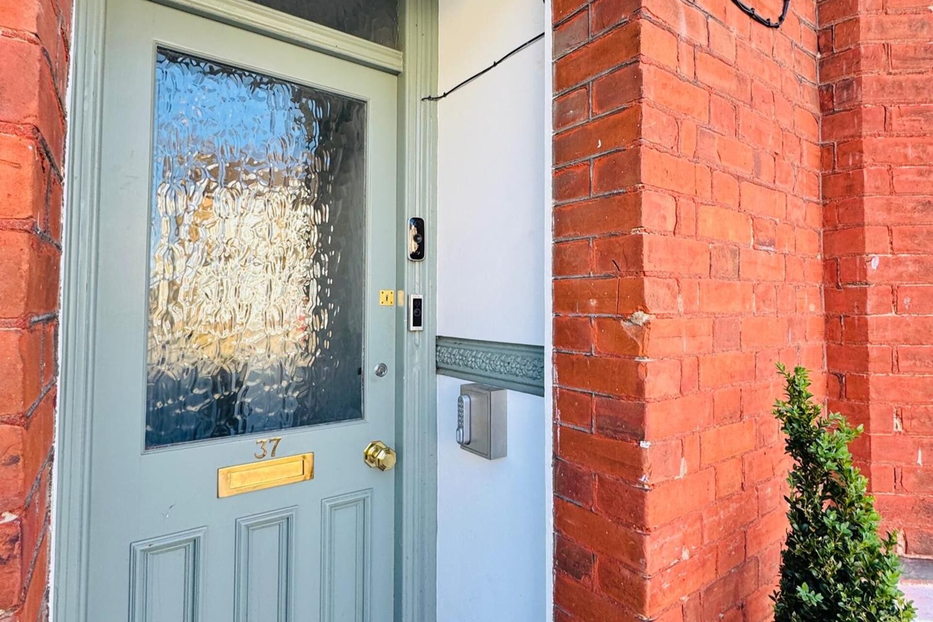 A door with a glass panel, a brass doorbell, and a mailbox on the wall.