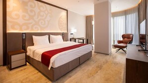 Quarto de hotel com uma cama grande, uma escrivaninha, uma cadeira e uma televisão.