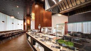 Disposição de buffet com diversos pontos de comida, área de estar com mesas e cadeiras, e cozinha moderna.
