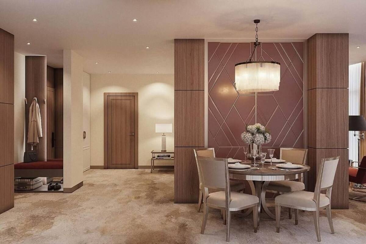 A hotel room with a dining area featuring a round table, chairs, a chandelier, and a wall with geometric patterns.
