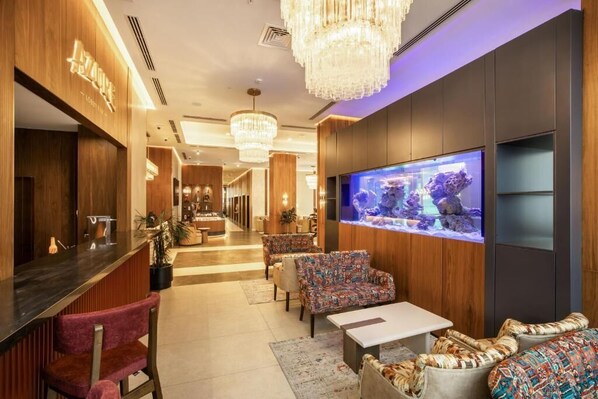 A lobby with a reception desk, seating area, and a large aquarium. - Zumma Hotel (Almaty)