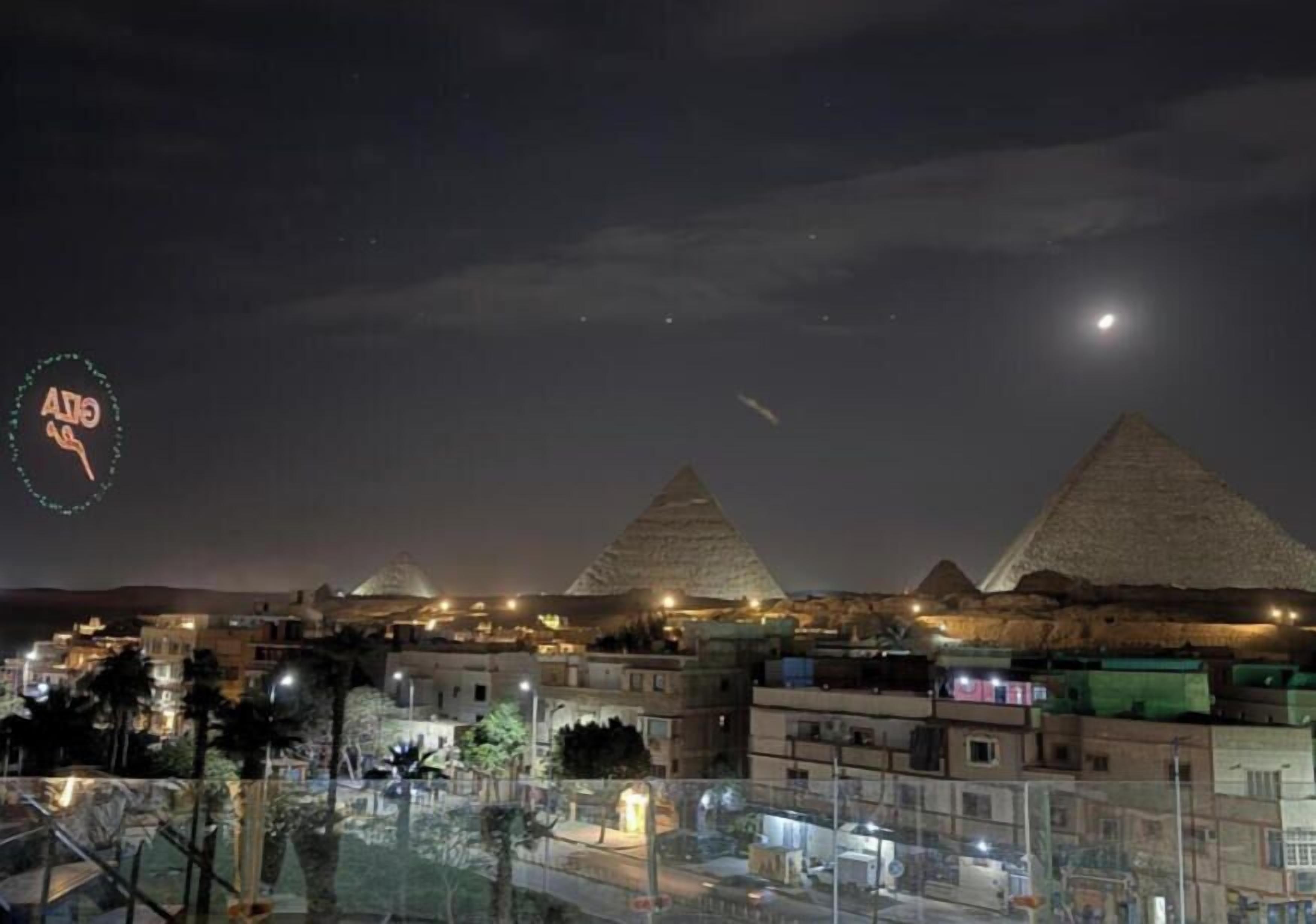 A nighttime view of the pyramids with surrounding buildings and a clear sky.