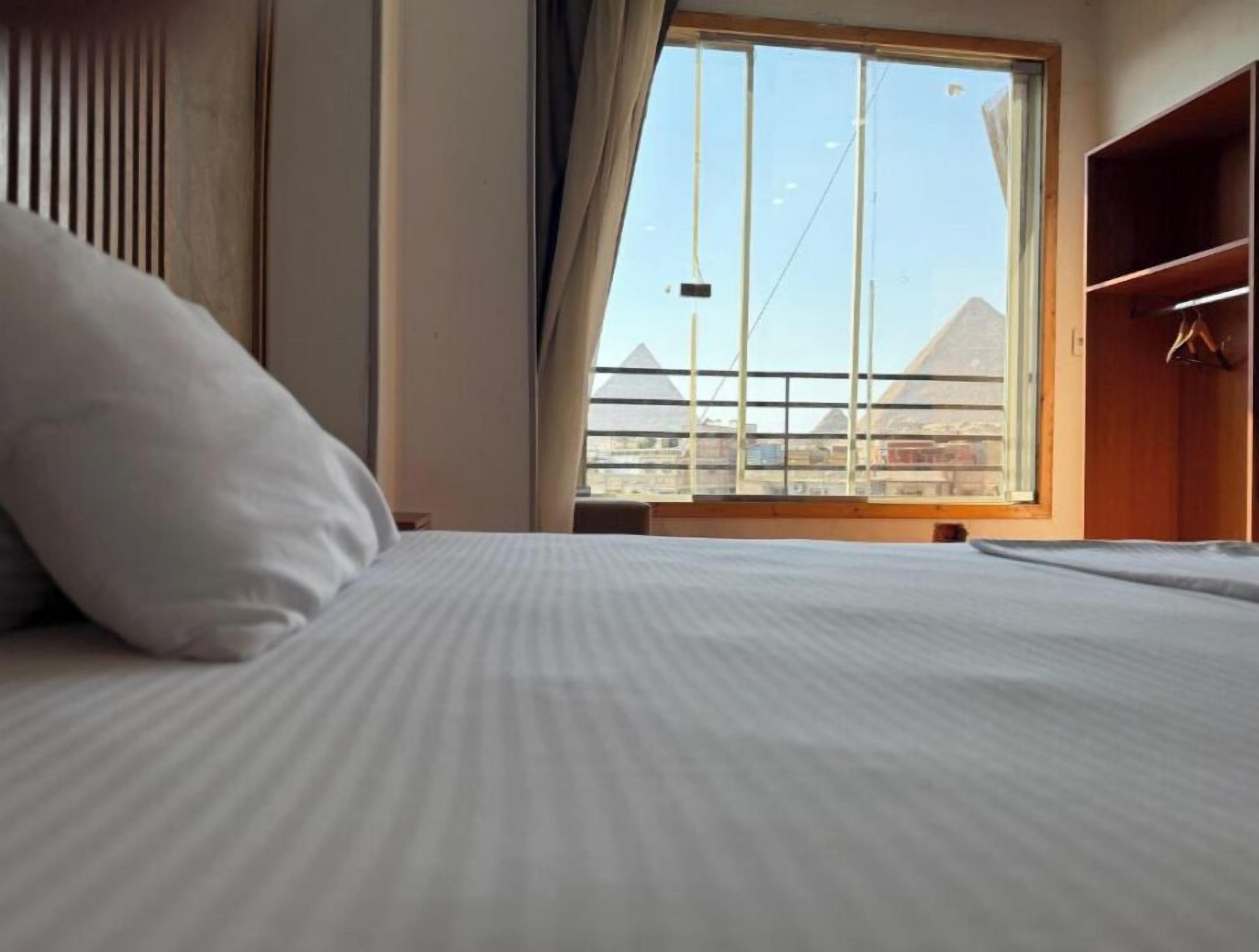 Habitación de hotel con cama, ventana que ofrece vistas a pirámides y armario.
