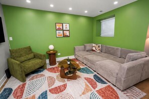 A living room with green walls, a grey sofa, a green armchair, a coffee table, and a patterned rug.