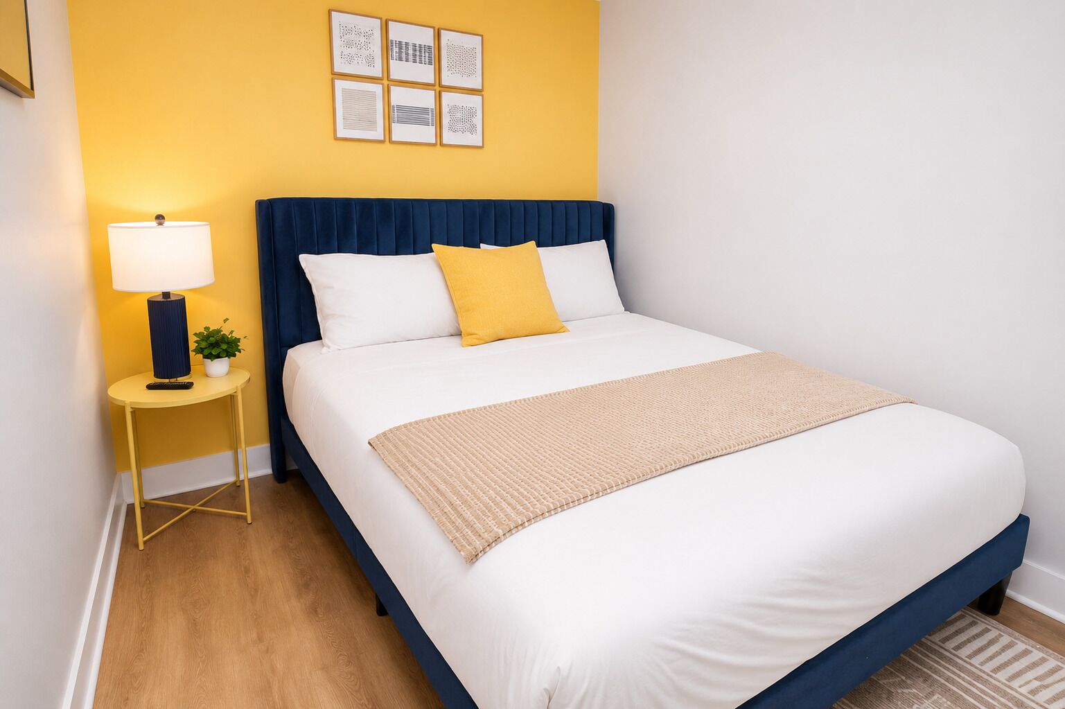 A neatly made bed with white and yellow bedding, a blue headboard, and a small bedside table with a lamp and a plant.