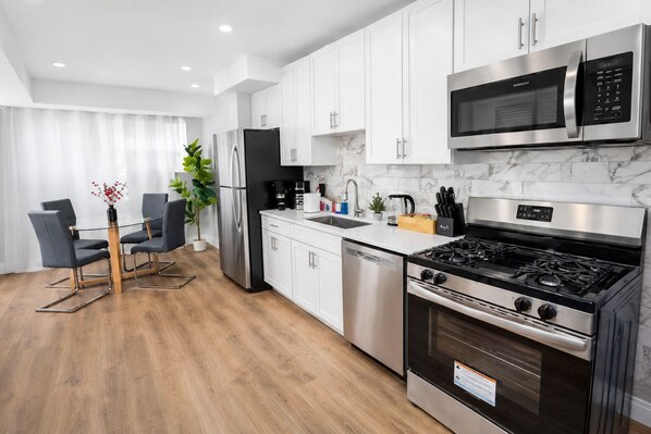 A modern kitchen with white cabinets, stainless steel appliances, a dining area with a table and chairs, and a potted plant.